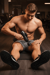 Athlete seated using massage gun on thigh grey shorts
